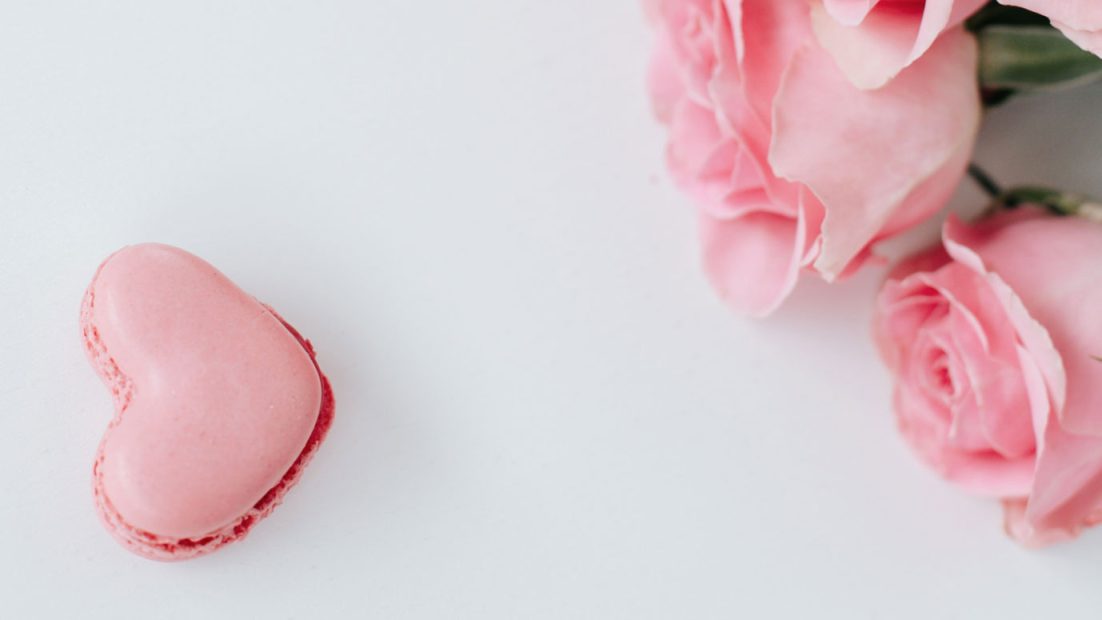 Un macaron en forme de coeur et des fleurs roses parce qu'il est important de faire de son mieux selon les 4 accords Toltèques