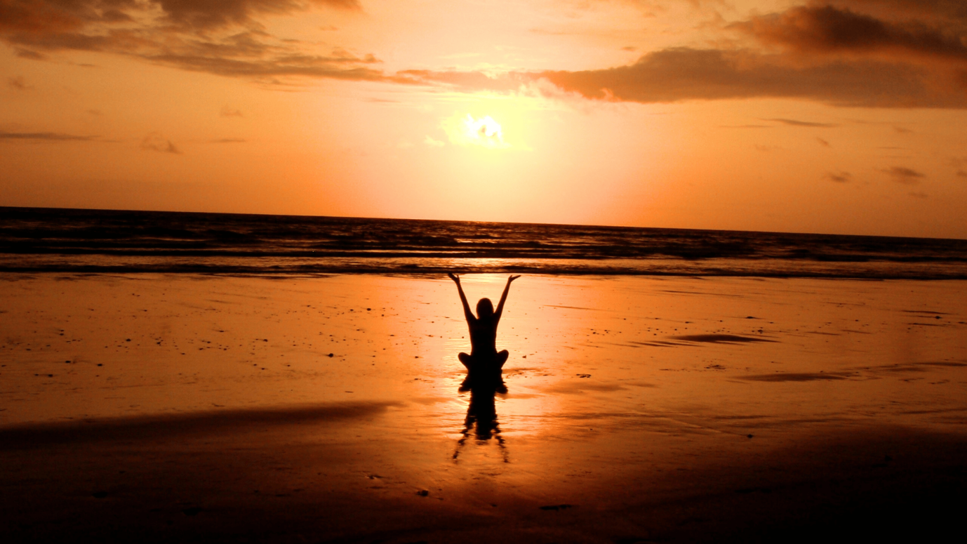 Une femme qui pratique la cohérence cardiaque sur la plage au coucher du soleil